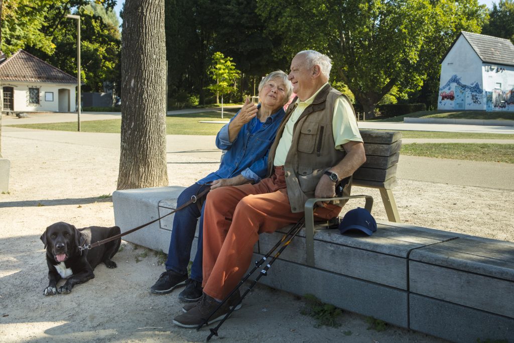 Ein altes Pärchen sitzt auf einer Bank auf der Insel Grafenwerth gemeinsam mit ihrem Hund.