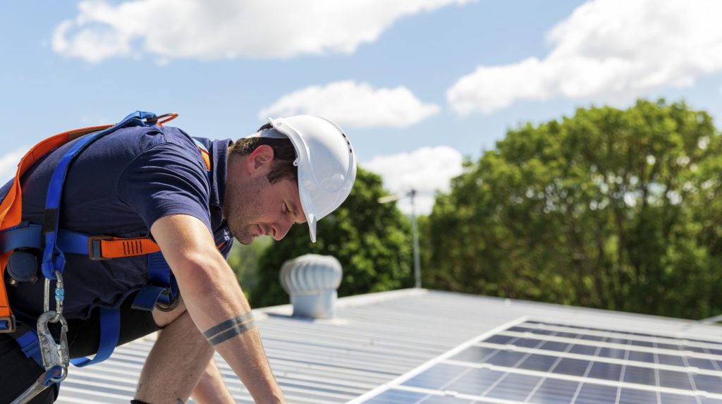 Mann befestigt auf einem Dach seine PV-Anlage.