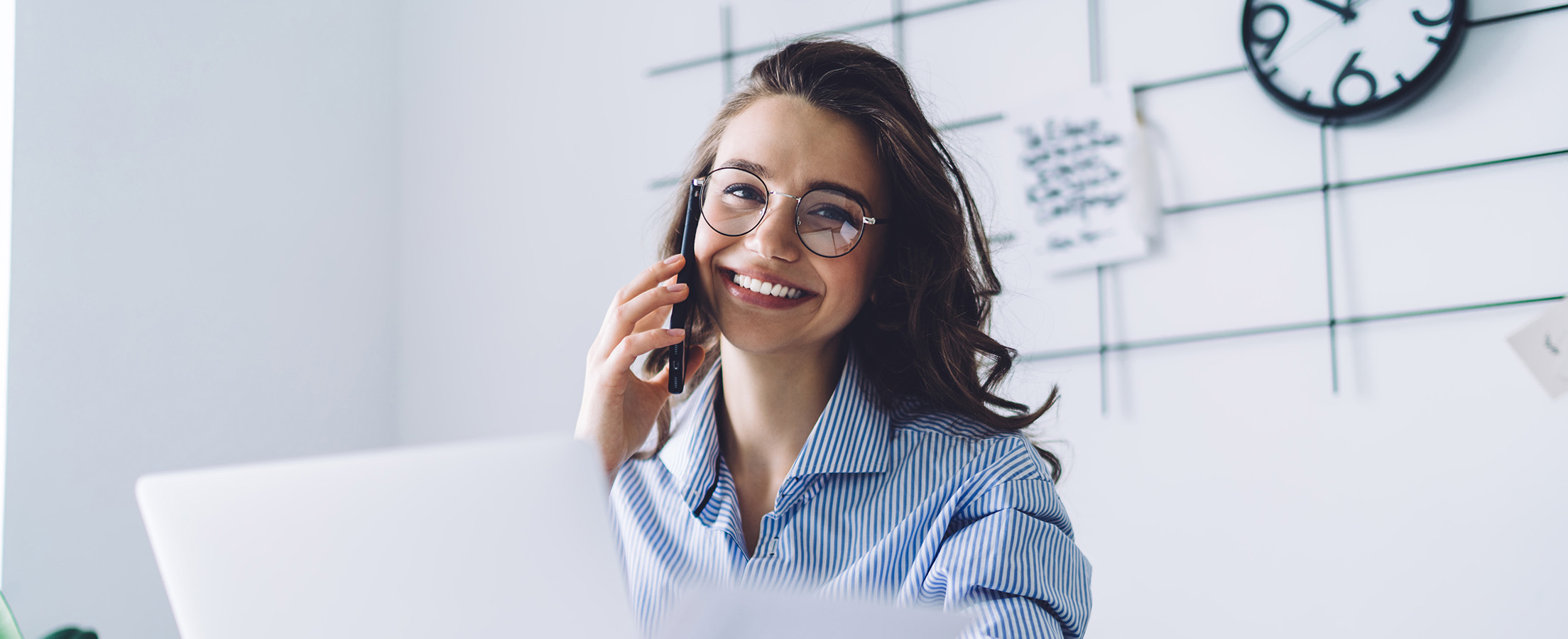 Frau sitzt im Büro und telefoniert mit ihrem Handy.