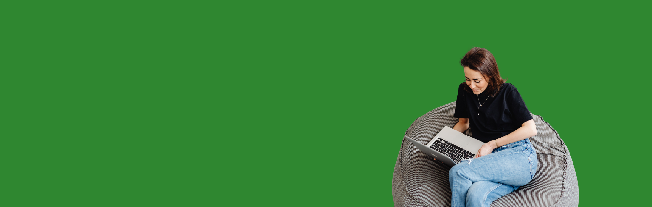 Frau mit Laptop sitzt auf Sitzsack vor einem grünen Hintergrund.