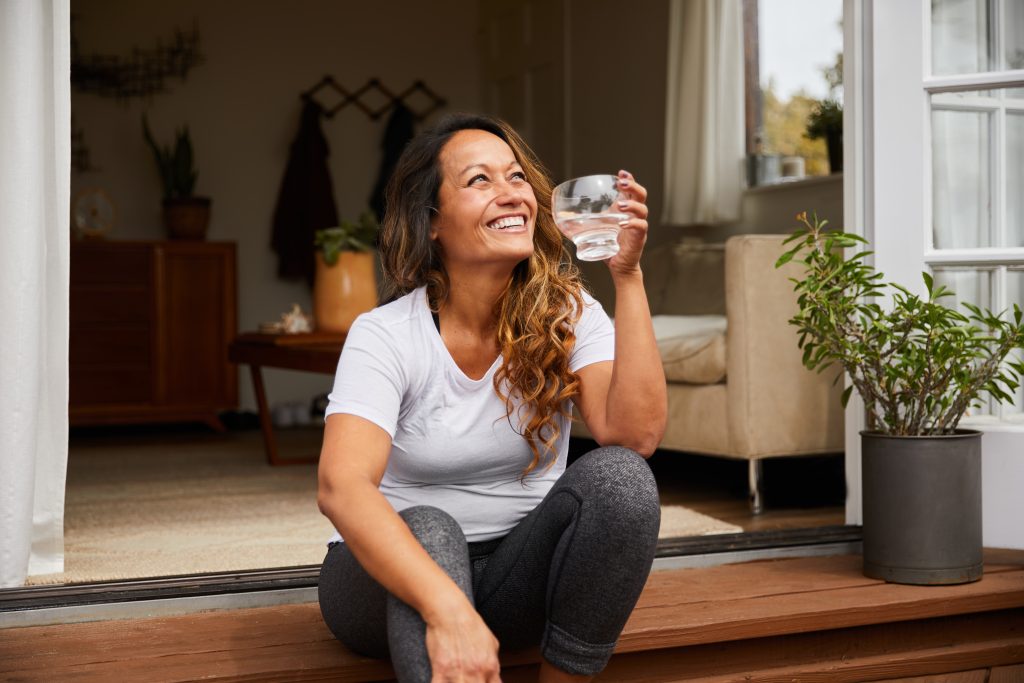 Lächelnde Frau sitzt auf einer Stufe mit einem Glas Wasser in der Hand.