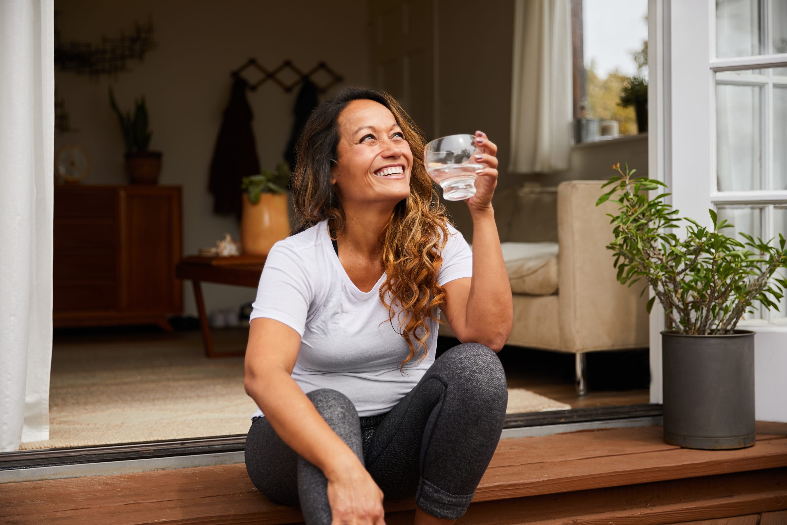 Lächelnde Frau sitzt auf einer Stufe mit einem Glas Wasser in der Hand.