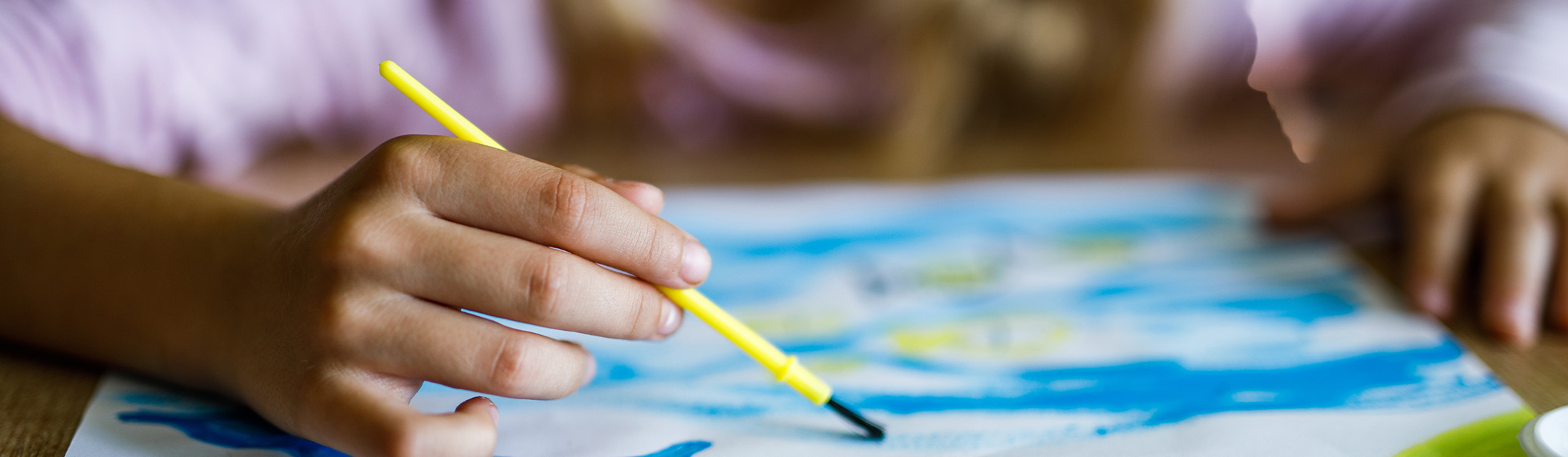 Kind malt mit Pinsel ein buntes Bild.