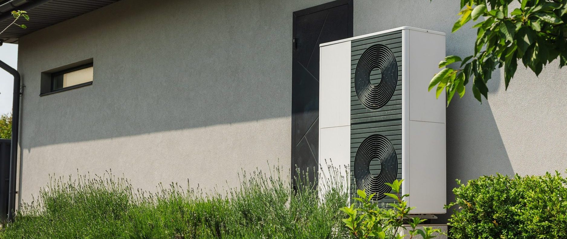 Wärmepumpe an einer Hauswand in einem Garten.